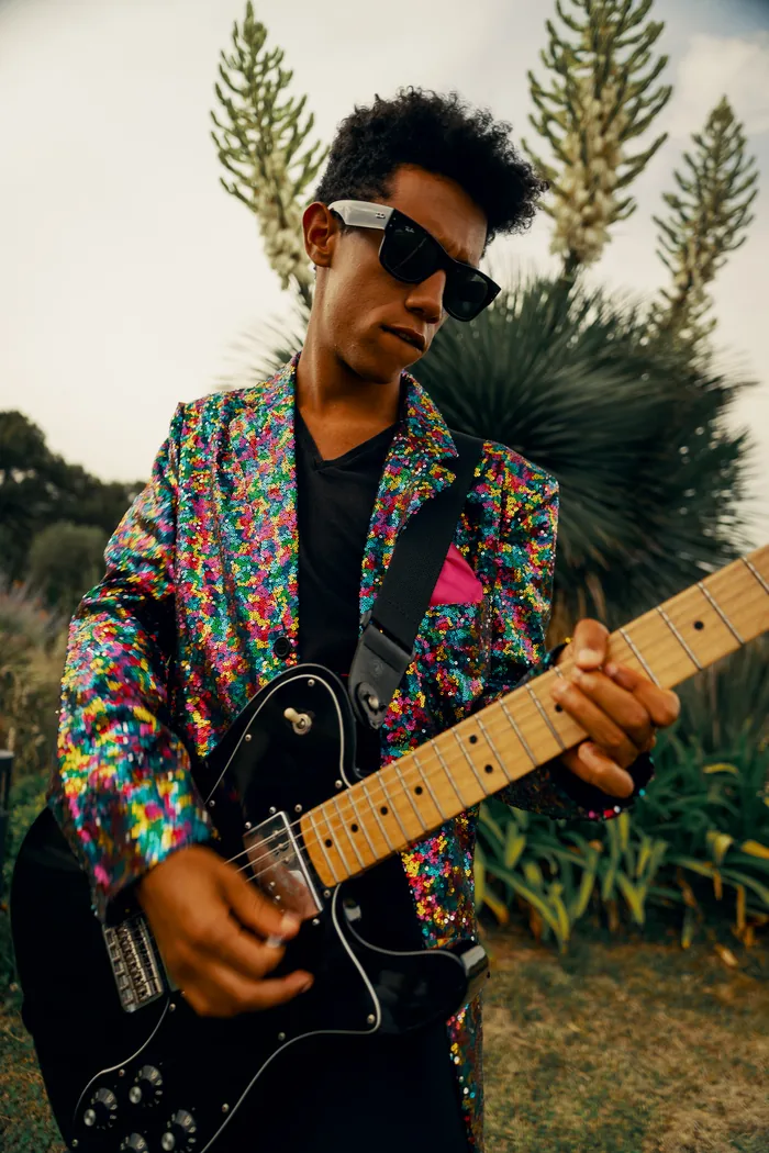 A Thrillers guitarist in a multicolour sequin jacket and sunglasses playing electric guitar