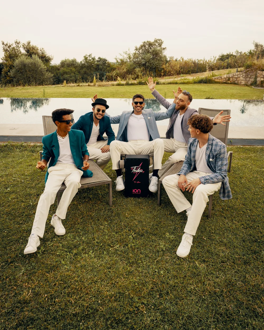 All five members of The Thrillers laughing with their arms up in light suits around their cajon